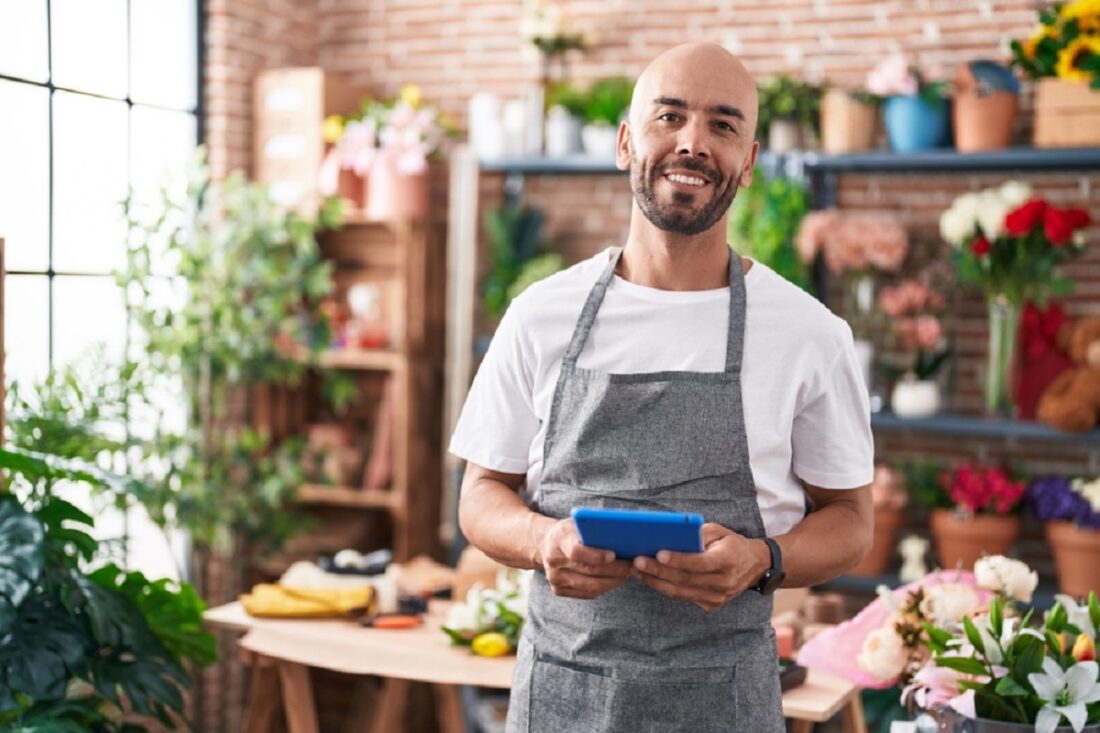 Young,Bald,Man,Florist,Smiling,Confident,Using,Touchpad,At,Florist