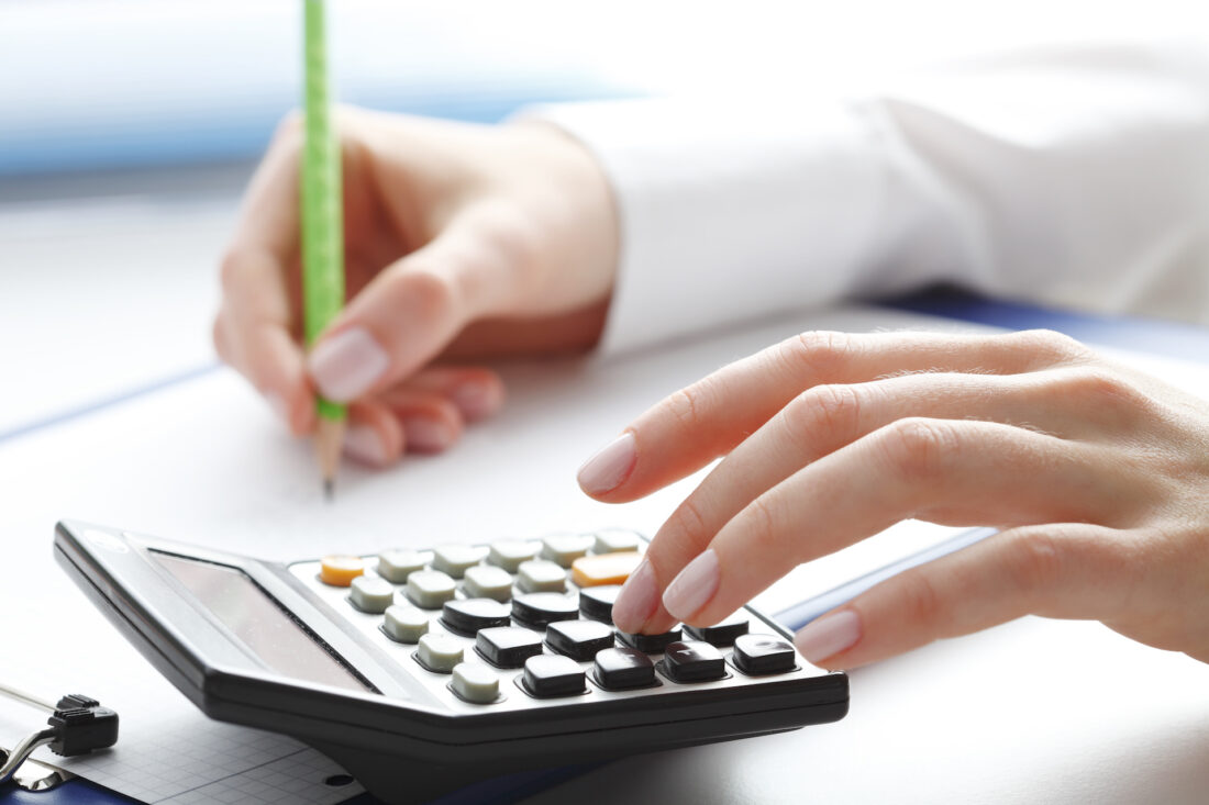 Financial data analyzing. Close-up photo of a businesswoman's hand writing and counting on calculator in office.  Selective focus