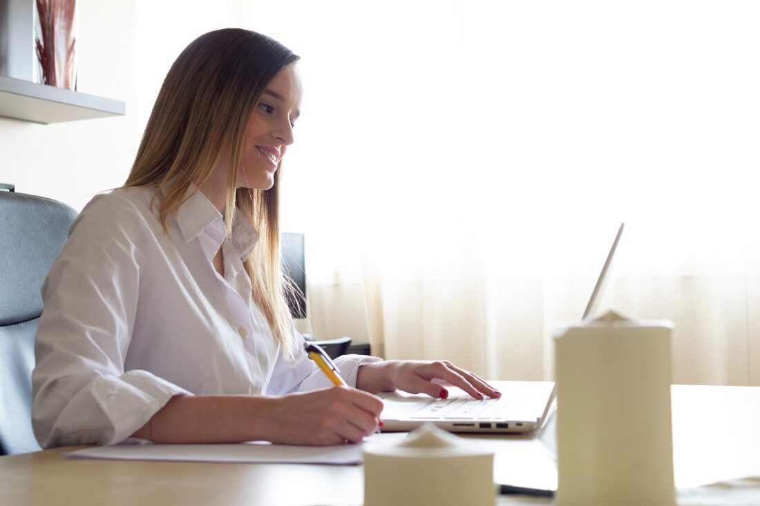 Young,Businesswoman,Teleworking,Sitting,At,A,Desk,Writing,And,Typing