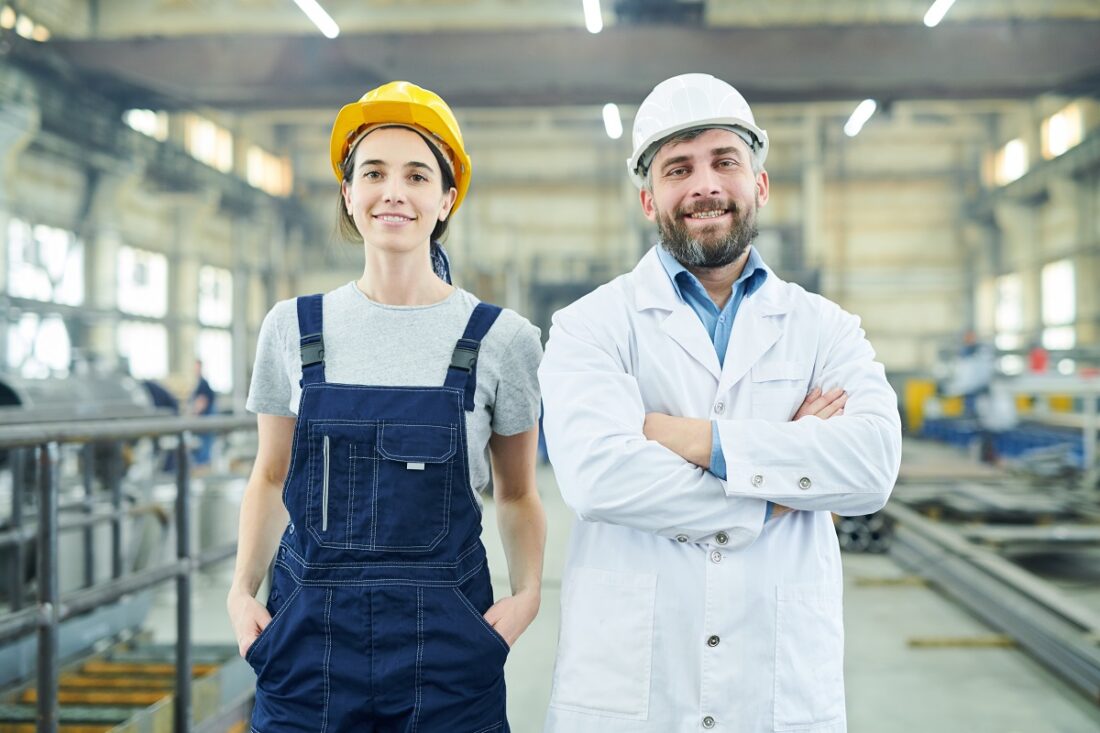 Waist,Up,Portrait,Of,Two,Smiling,Factory,Workers,Looking,At