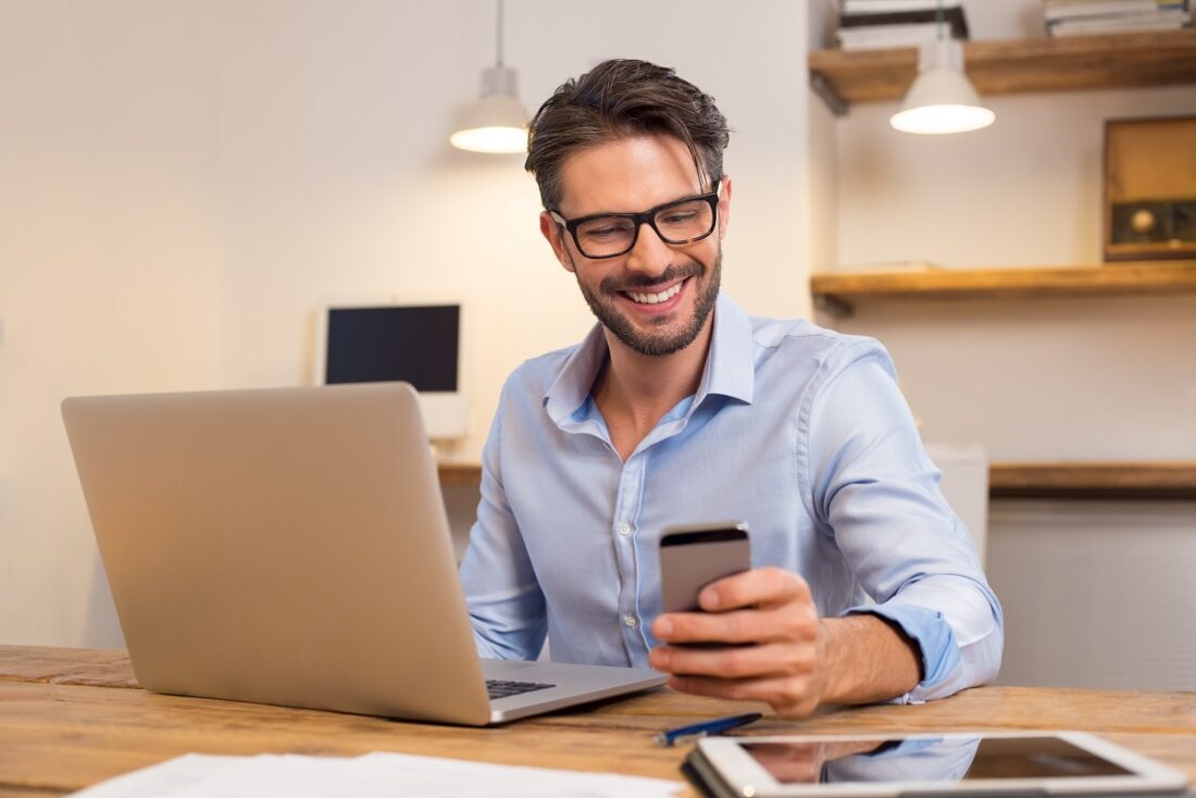 Young,Happy,Businessman,Smiling,While,Reading,His,Smartphone.,Portrait,Of