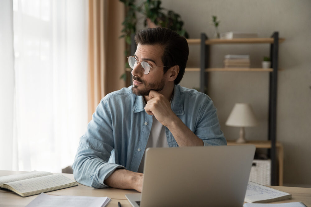 Pensive,Young,Guy,Employee,Sit,At,Workplace,Look,Aside,Of