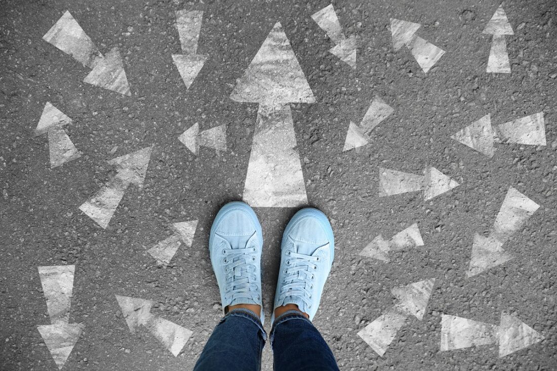 Woman,Standing,On,Asphalt,Road,With,Arrows,Pointing,In,Different