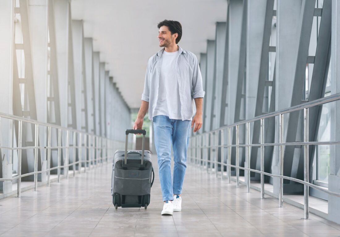 Young,Man,Walking,In,Airport,Walkway,With,Luggage,,Free,Space