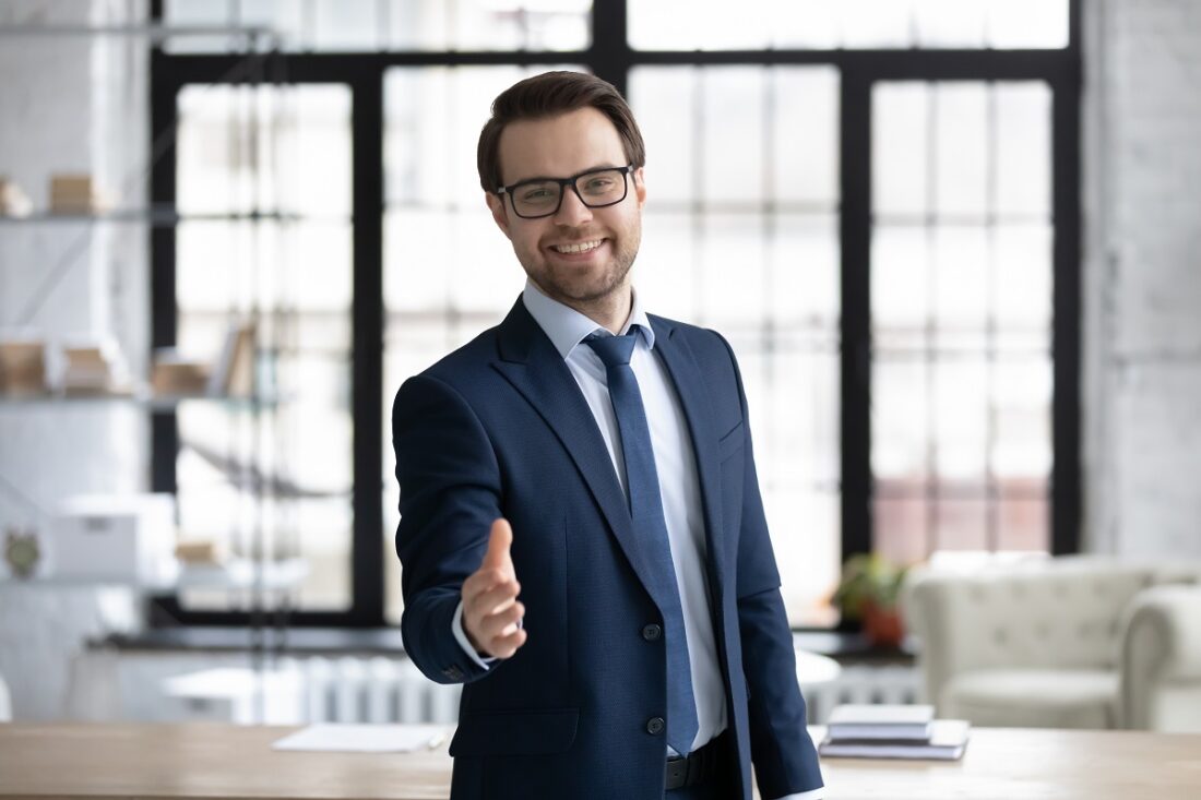 Happy,Young,Businessman,In,Glasses,Looking,At,Camera,,Reaching,Out