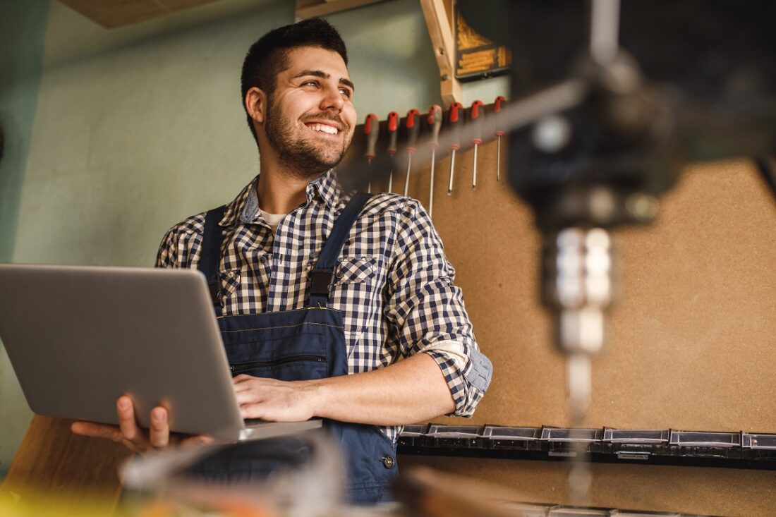 Shot,Of,A,Smiling,Carpenter,Using,Laptop,At,Work,In