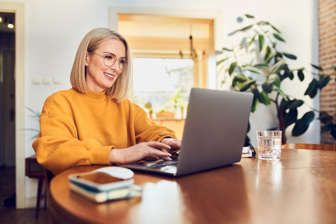 Portrait,Of,Middle,Aged,Woman,Sitting,At,Dinning,With,Laptop