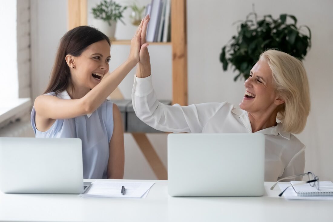 Cheerful,Middle-aged,And,Millennial,Women,Colleagues,Seated,At,Workplace,Desk